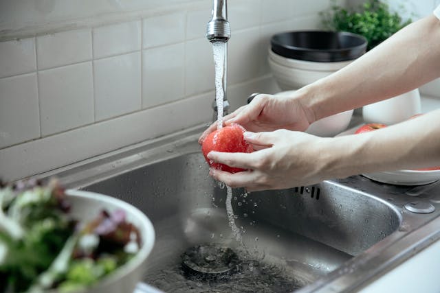 person washing fruit under kitchen faucet