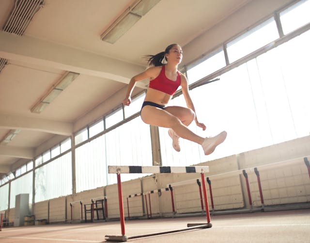 woman in workout gear jumping over a hurdle