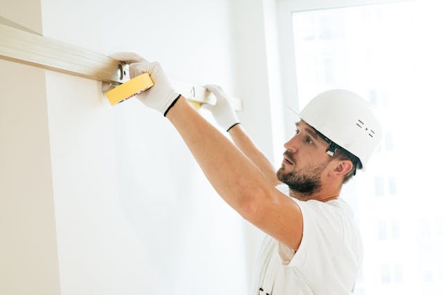 man in white work clothes using a level