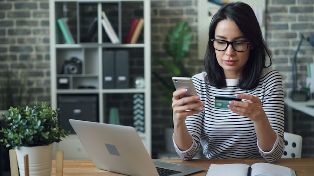 woman sitting and looking at phone and credit card