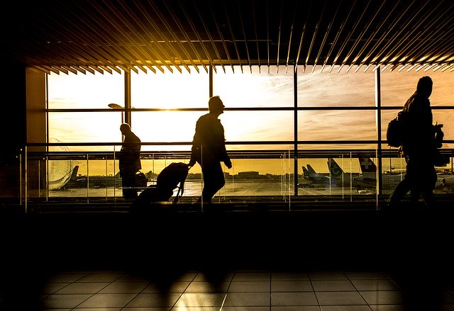 person in airport pulling suitcase with sunrise behind through the windows
