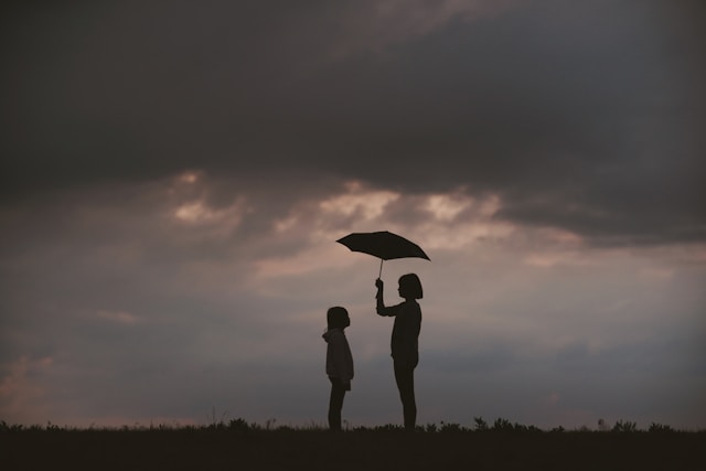 silhouette of woman holding umbrella over a child with cloud sky in background