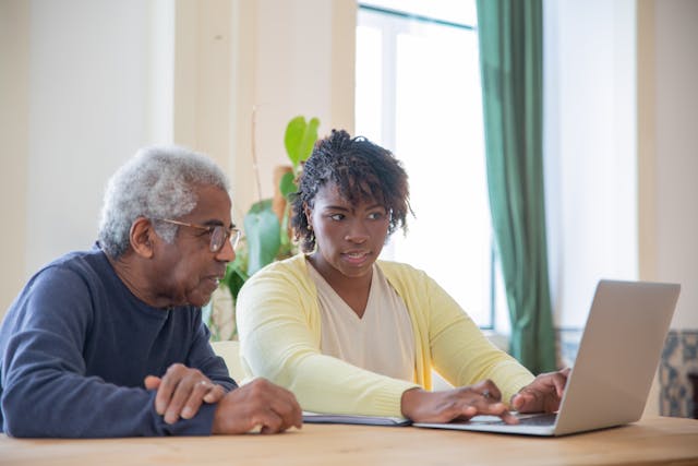 elderly man and younger woman using laptop together