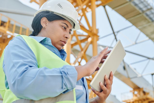 female construction worker in hardhat using touchscreen device