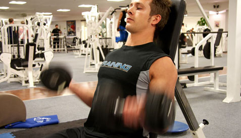 man in gym sitting and doing curls with dumbells