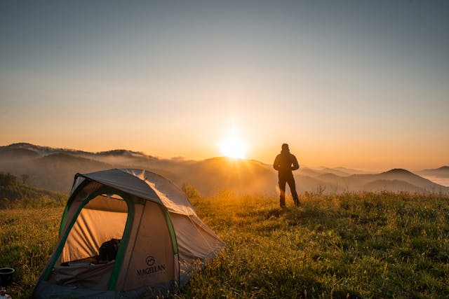 silhouette of a person looking at the rising sun with camping tent nearby