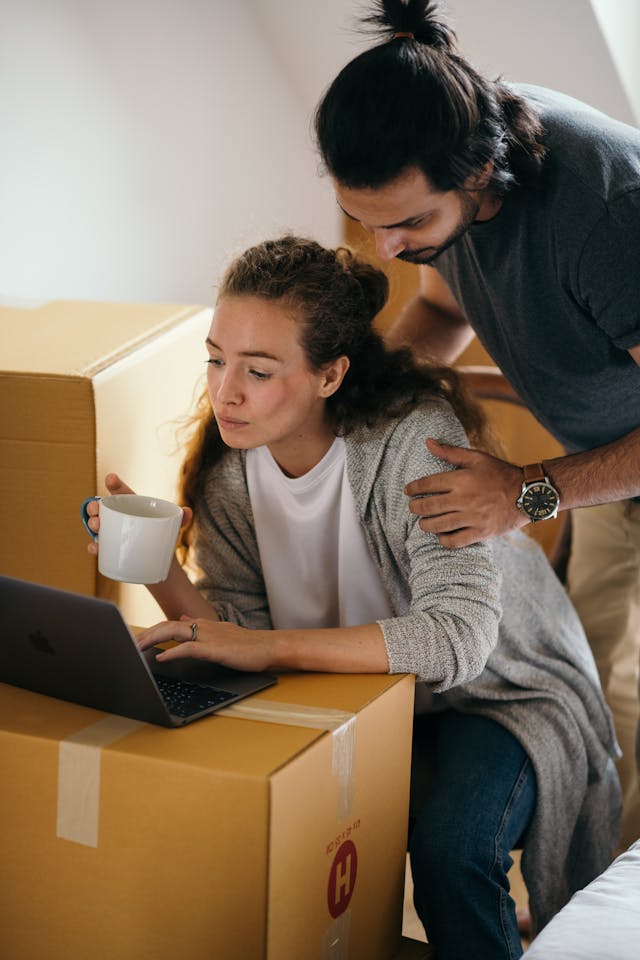 young couple using laptop and surrounded by boxes in a room