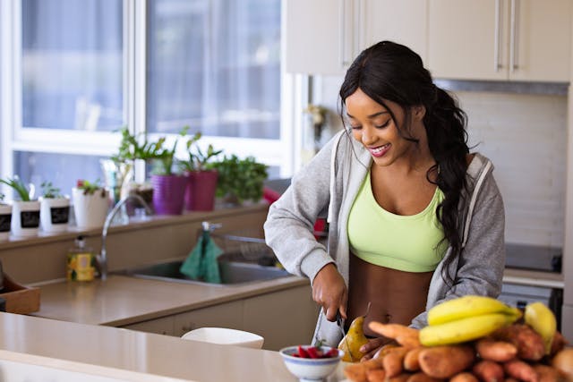 pretty brunette woman with caramel skin in shirt and lime green tank top slicing veggies in kitchen