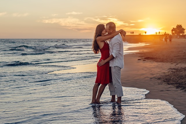 romantic embrace by couple standing on the edge of the beach with the sun setting in the backgroun