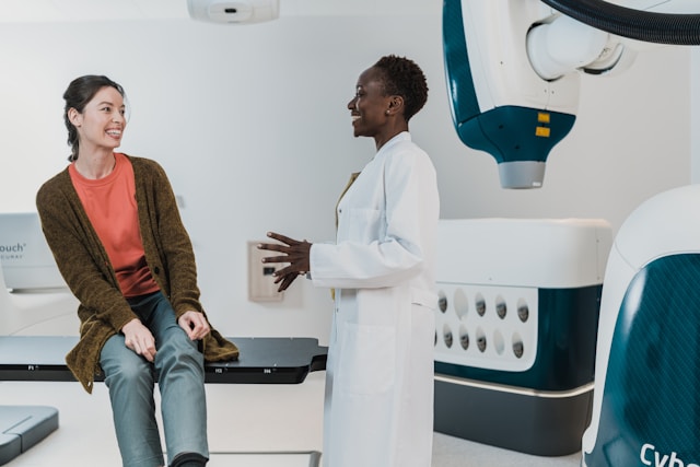 female doctor in white coat speaking with female patient sitting on exaamining table
