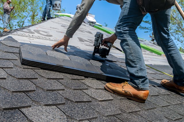 closeup of roofer standing on roof installing shingle