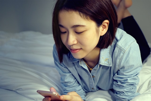 pretty asain woman laying on bed looking at her smartphone