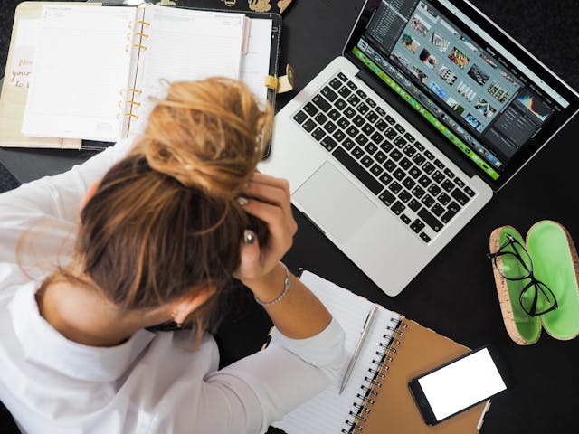 overhead view of blond woman sitting at desk with laptop with face in hands
