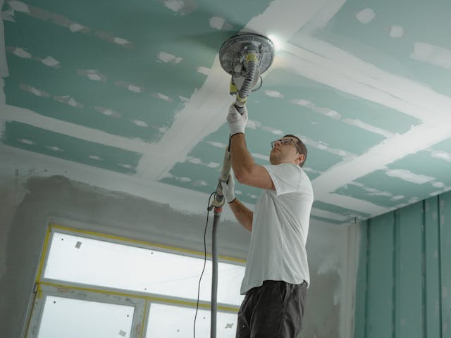 man using electric sander on ceiling during home renovation
