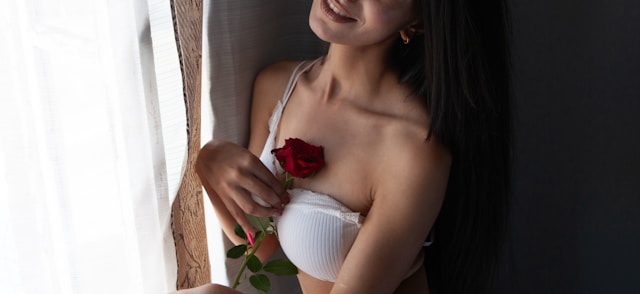 closeup of a red rose held by a beautiful brunette woman wearing a sexy white bra with a strap down