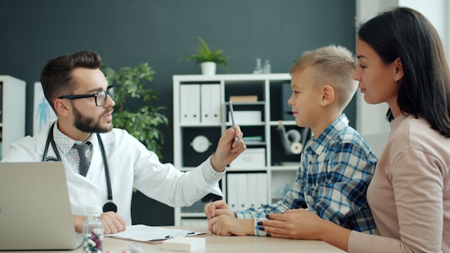 doctor examining young boy with attractive mother looking on