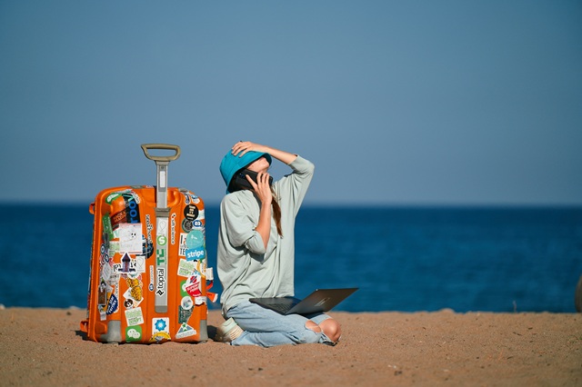 woman on the beach with luggage on phone with laptop