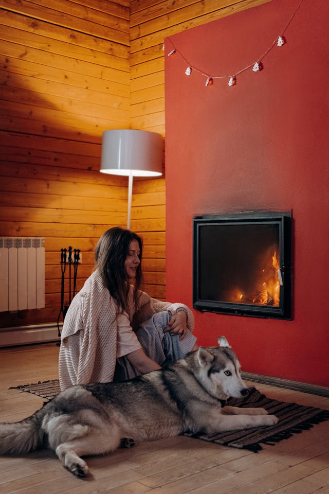 pretty brunette woman with blanket sitting by fireplace with her dog