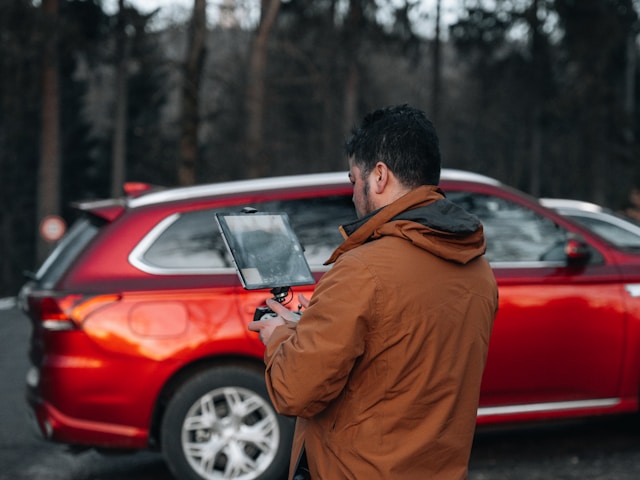 man with laptop by red car