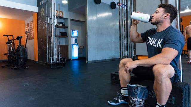 man in gym sitting on bench drinking from water bottle