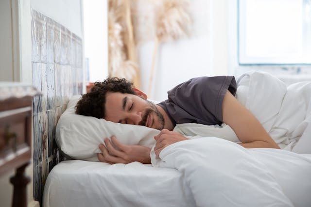 man sleeping inbed in t-shirt with white sheets