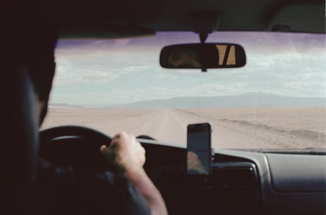 view of man driving car over his shoulder looking out onto the road