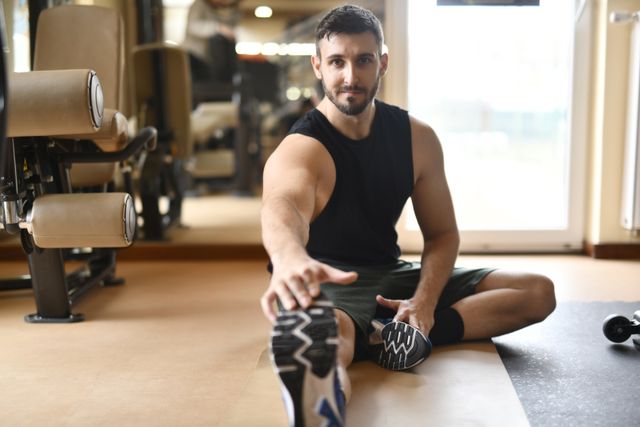 man in black tank top and sneakers stretching on floor