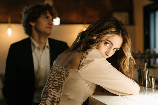 pretty woman with brown hair looking over her shoulder at bar with man in background