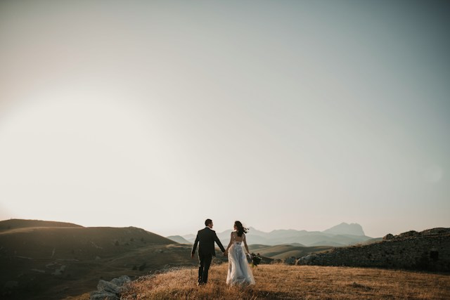 bride and groom holding hands in outdoor setting rear view