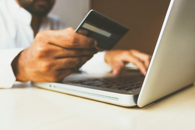 man holding credit card while typing into laptop
