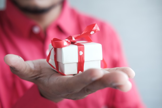 man holding small white gift box with red bow