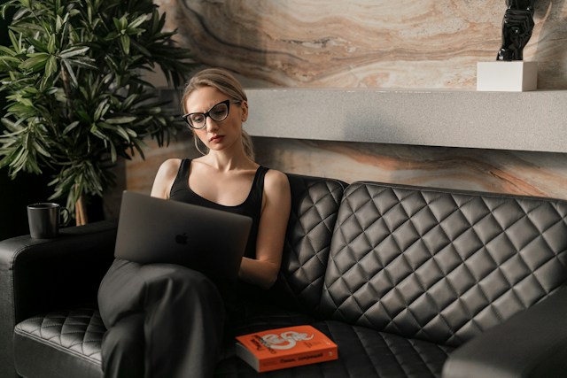 pretty blonde professional woman on couch using laptop with book next to her on couch