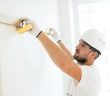 man in white work clothes using a level