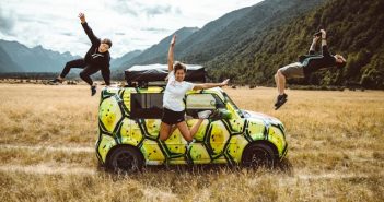 men and women jumping around a car