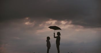 silhouette of woman holding umbrella over a child with cloud sky in background