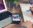 man writing on pad on desk with laptop and smartphone