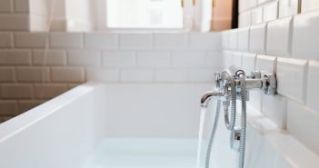 steel faucet and bathtub with ceramic tiles on wall