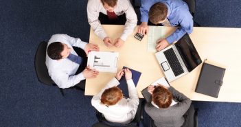 ariel view of people sitting at desk at work with laptop