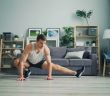 man in white tank top and black shorts and sneakers doing stretching in living room