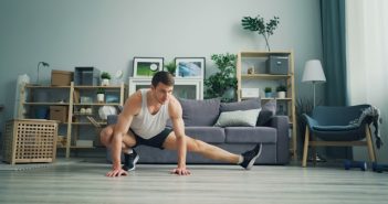 man in white tank top and black shorts and sneakers doing stretching in living room