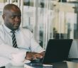 man in white shirt and tie in office working on laptop with coffee cup