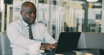 man in white shirt and tie in office working on laptop with coffee cup