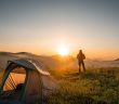 silhouette of a person looking at the rising sun with camping tent nearby
