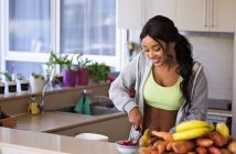 pretty brunette woman with caramel skin in shirt and lime green tank top slicing veggies in kitchen