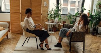 woman sitting on a chair talking to female therapist also sitting on the chair across from her