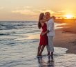 romantic embrace by couple standing on the edge of the beach with the sun setting in the backgroun