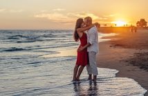 romantic embrace by couple standing on the edge of the beach with the sun setting in the backgroun