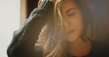 closeup of pretty woman with brown hari in dark green sweater with her eyes closed