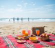 picnic food on blankett on the beach with peple far in the background
