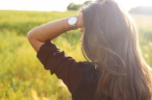 rear view of woman with long dark hair with hand in her hair weraing gold watch
